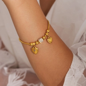 Goldenes Schlangenarmband mit Herzanhängern und funkelnden Strasssteinen am Handgelenk