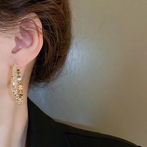 Gros plan de boucles d'oreilles créoles dorées en C avec zircons portées par un mannequin