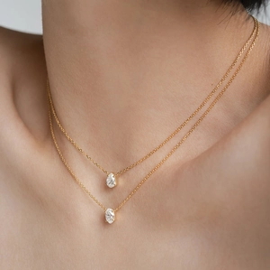 Macro close-up of double-layer gold chain necklace with pear and oval stone pendants