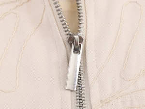 Detail of silver metal zipper on cream-colored fabric with delicate wave embroidery