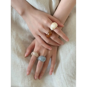 Model wearing various marbled resin oval rings on neutral linen background for styling