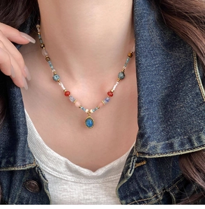 Détail d'un collier de perles colorées avec pendentif bleu sur chemise en jean