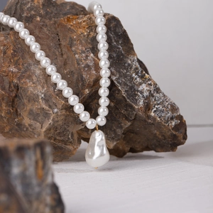 Dettaglio della collana di perle bianche con pendente barocco su una roccia minerale