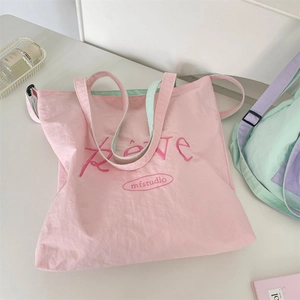 Detail of pink canvas tote bag with green straps and Rêve embroidery in top-down view