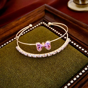 Detailed shot of double-layered gold bow bracelet with pink heart stones and zircons