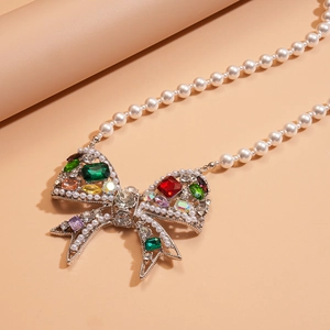 Luxe pearl necklace with a colorful gemstone-encrusted bow pendant on pink background