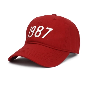 Classic red cotton baseball cap with white 1987 embroidery and curved brim in side view