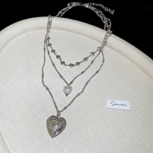 Detailed view of triple-layered silver heart pendant necklace with pearl charm detail