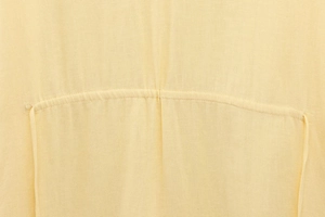 Macro view of light yellow woven linen fabric texture and detailed stitching on shirt