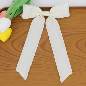 Detail of white silk bow hair clip with long streamers on a rustic wooden tray