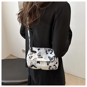 Side view of white crossbody bag with black butterfly prints worn by a model