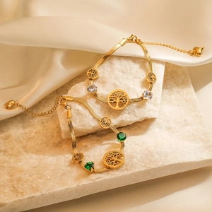 Goldenes Lebensbaum-Armband mit Smaragd- und Zirkonia-Steinen auf weißem Naturstein