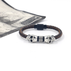 Detail of dark brown braided leather bracelet with silver skull charm and black magnetic clasp