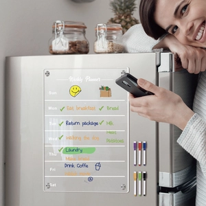 A woman using the clear acrylic weekly planner board with markers on a refrigerator