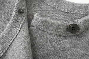 Dettaglio cappotto in maglia grigia con texture morbida e bottoni neri rotondi eleganti