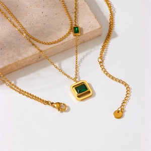 Elegant gold double layer necklace with square green gemstones on a white stone background
