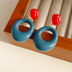 Detailed view of red and blue resin earrings with golden metal links in a jewelry box