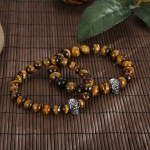 Detailed view of beaded tiger eye bracelets with metal skulls on dark bamboo mat