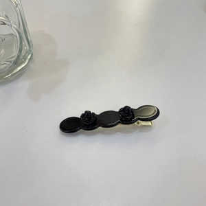 Detail view of twin black acetate rose flowers on a gold-tone metallic hair duckbill clip