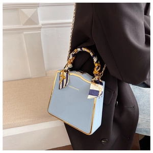 Detail of light blue box bag with gold metal trim and silk scarf wrapped handle