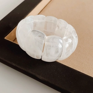 Macro shot of wide acrylic stretch bracelet with white marble texture beads on suede