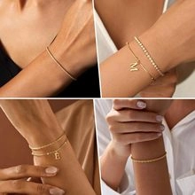 Détail de bracelets à chaîne dorée superposés avec lettres E et M et zircons brillants