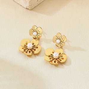 Macro shot of gold hollow petal earrings featuring elegant white pearls on stone surface