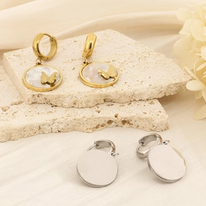 Golden butterfly shell earrings and silver circular studs on a decorative stone base