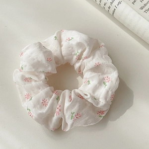 Close-up of floral scrunchie with pink flowers on white fabric beside an open book