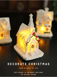 Macro shot of glowing white resin Christmas house with warm LED lights and festive text