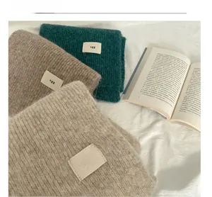 Detail of wool-blend knitted scarves in green, brown and beige with woven egg labels