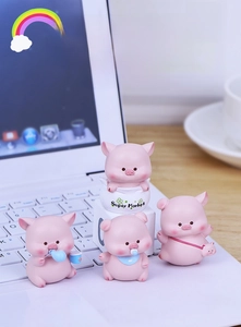 Miniature pink resin pig figurines displayed on a laptop keyboard as office decor