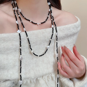 Detail of beaded star and pearl necklace with heart charms over a white sweater
