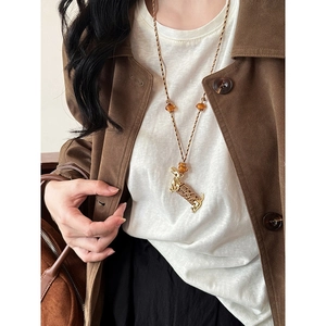 Détail du pendentif teckel doré sur un collier en corde tressée porté par un mannequin