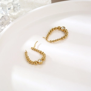 Macro shot of gold beaded earrings with sparkling oval gems on a white ceramic plate