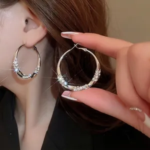 Silver-plated twisted hoop earrings with shimmering rhinestones worn by a model