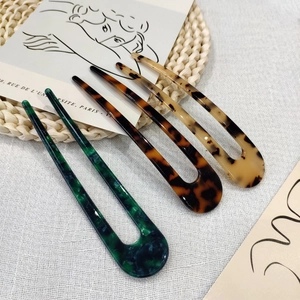 Detailed view of three acetate U-shaped hair pins in green and amber tortoise patterns