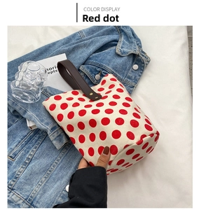 Close-up of red polka dot canvas bucket bag with brown leather handles and metal rivets
