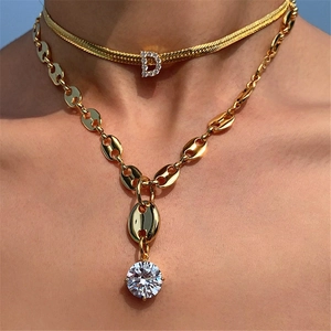 Detail of layered gold snake chain with D pendant and round zircon solitaire necklace