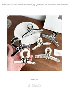 Close-up of resin bow hair claw clips in black and cream with Grace script logo
