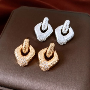 Detail view of gold and silver geometric earrings with brushed metal and white zircon