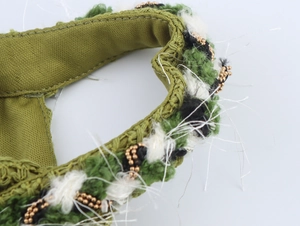 Detailed close-up of the elegant olive green fabric with intricate woven beadwork and white fringe