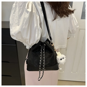 Detail view of black bucket bag with chain strap and plush pendant on female model