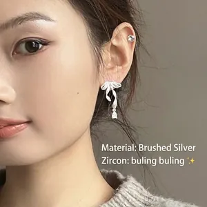 Brushed silver bow earrings with sparkling zircon teardrops worn by a female model