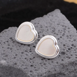 Minimalist heart-shaped stud earrings with white inlay on grey stone background