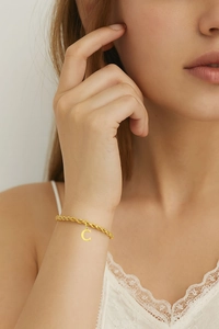 Dettaglio di un bracciale dorato con ciondolo lettera C e catena a corda sul polso