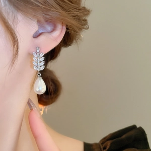 Elegant cubic zirconia leaf earrings with teardrop pearl pendants worn by a model