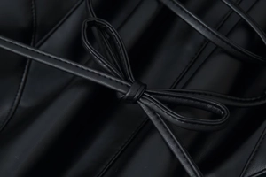 Détail de la texture cuir synthétique noir avec nœud décoratif à lacets sur la manche