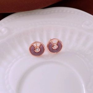 Close-up of rose gold earrings with purple enamel and zircon inlay on a white plate