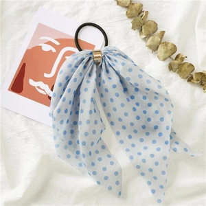 Detail of light blue polka dot bow hair tie with gold buckle on a white fabric surface